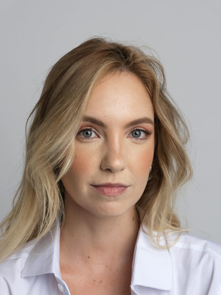 Close-up portrait of a blonde woman in a white shirt, looking confidently at the camera.